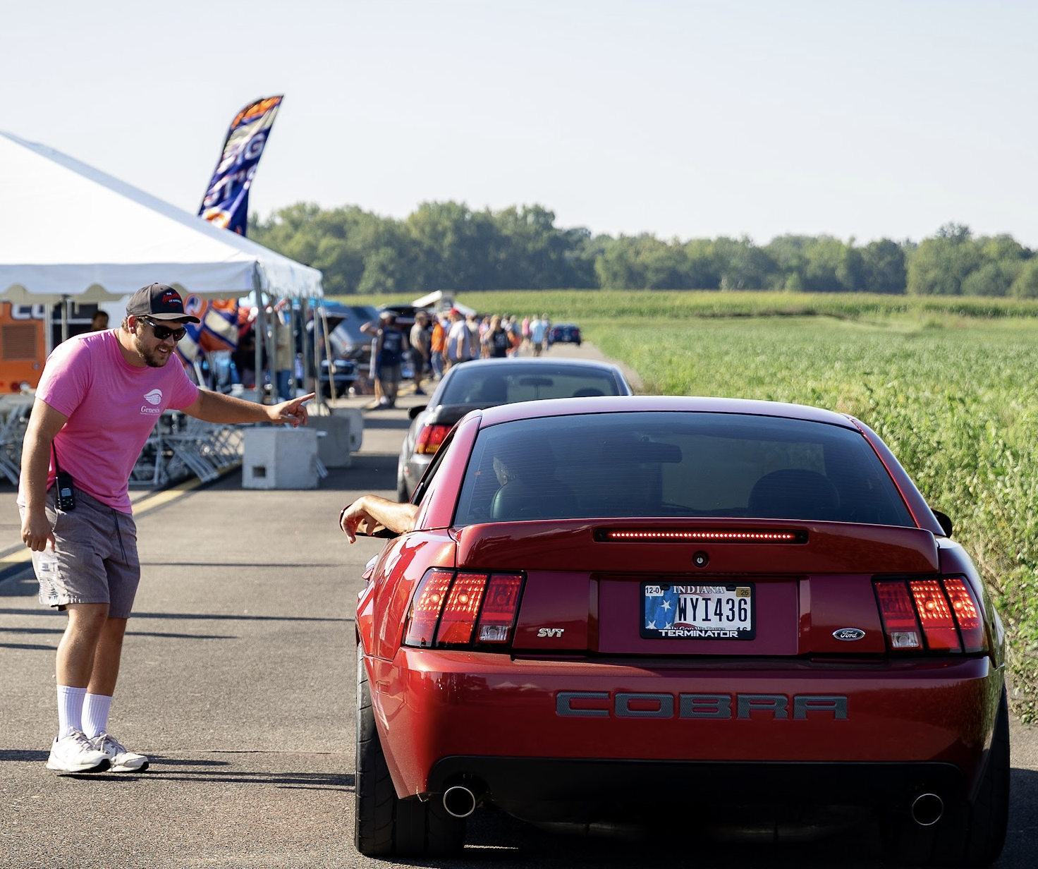 A Runway Classic volunteer directs a red Ford Mustang Cobra along the airport roadway.